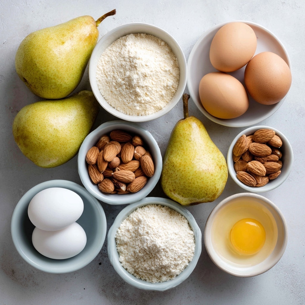 Overhead shot of fresh pears, eggs, almonds, flour, and almond meal in bowls on a white surface.