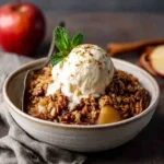 Bowl of vegan apple crisp topped with dairy-free ice cream and fresh mint.