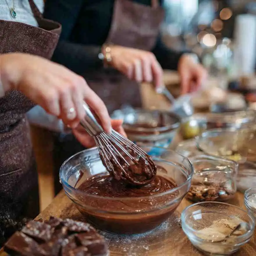 Hands whisking rich chocolate fudge batter in a glass bowl during holiday baking.