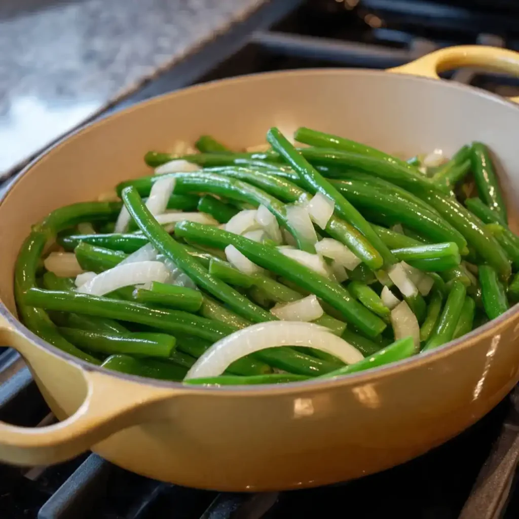 Fresh green beans and sliced onions cooking in a yellow Dutch oven on the stove.