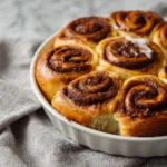 Golden cinnamon rolls from scratch baked together in a round pan with visible cinnamon swirls.