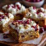Cranberry bliss bars topped with cream cheese frosting and cranberries on a wooden serving board.